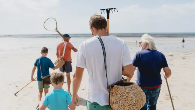 Eine Familie geht am Strand mit Werkzeugen zum Sammeln von Muscheln