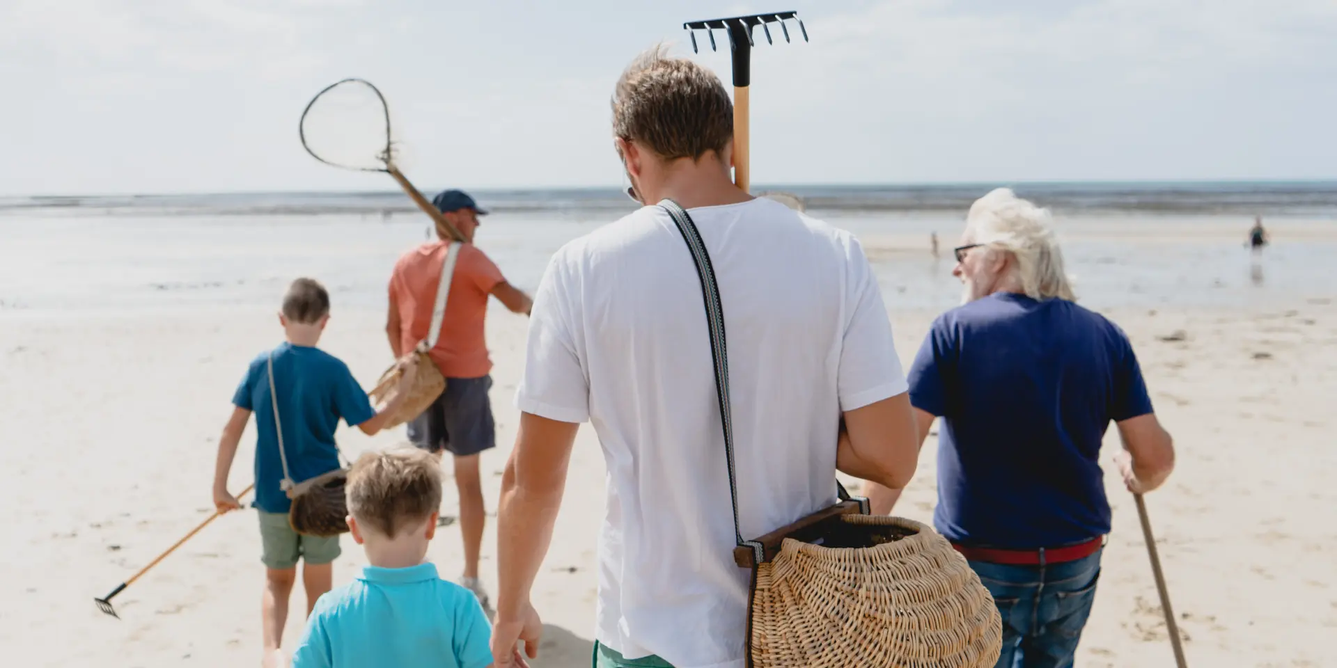 Eine Familie geht am Strand mit Werkzeugen zum Sammeln von Muscheln