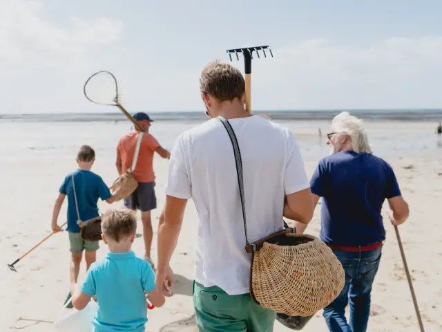 Eine Familie geht am Strand mit Werkzeugen zum Sammeln von Muscheln