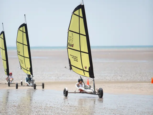 Three sailboats on a beach with people on board