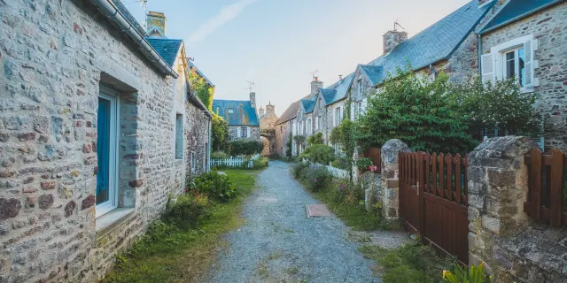 Rue pavée bordée de maisons en pierre avec des jardins bien entretenus