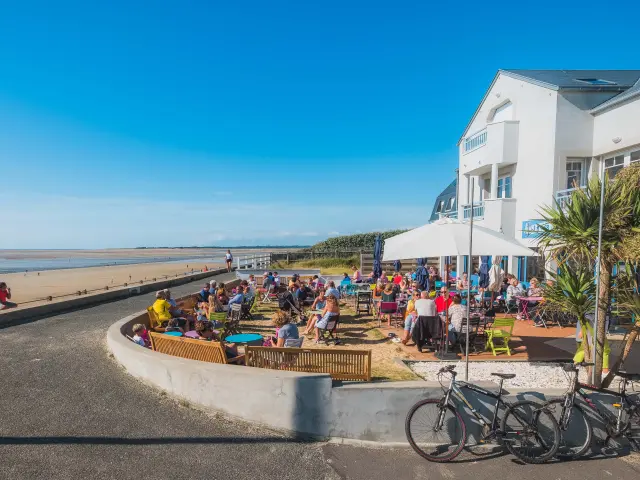 Terrasse de café bondée en bord de plage avec des gens assis et des vélos garés