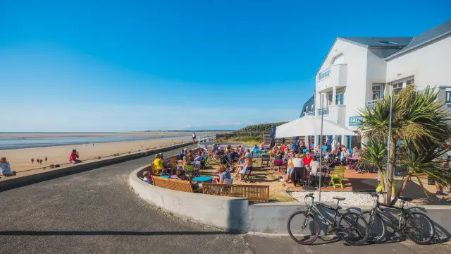Belebter Café-Terrasse am Strand mit Menschen, die sitzen und Fahrräder geparkt