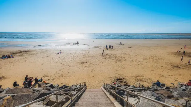 Treppen, die zu einem Sandstrand mit Menschen führen, die sich entspannen und am Wasser spielen