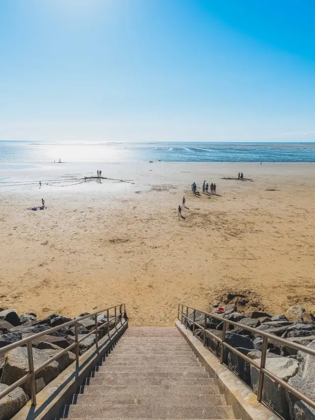 Escaliers menant à une plage de sable avec des gens se relaxant et jouant près de l'eau