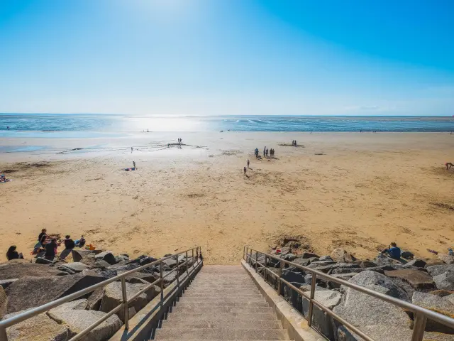 Treppen, die zu einem Sandstrand mit Menschen führen, die sich entspannen und am Wasser spielen
