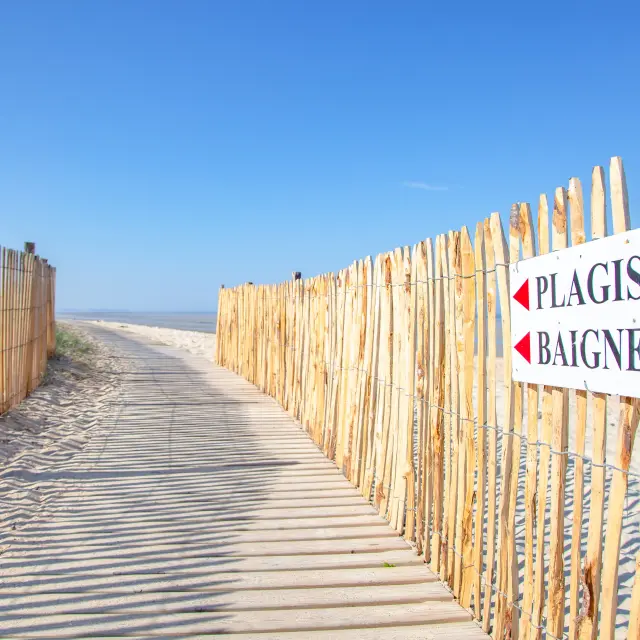Holzsteg, der zu einem Strand mit einem Schild führt, auf dem Rettungsschwimmer Badende steht