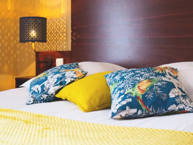 Bett mit bunten Kissen und einer Nachttischlampe