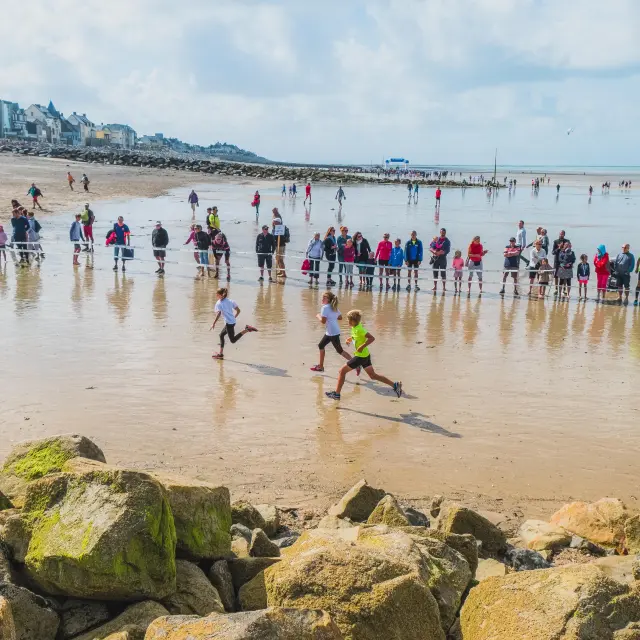 Participants courant sur une plage avec des spectateurs