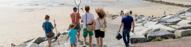 Une famille marche sur une plage avec des enfants tenant des filets à papillons