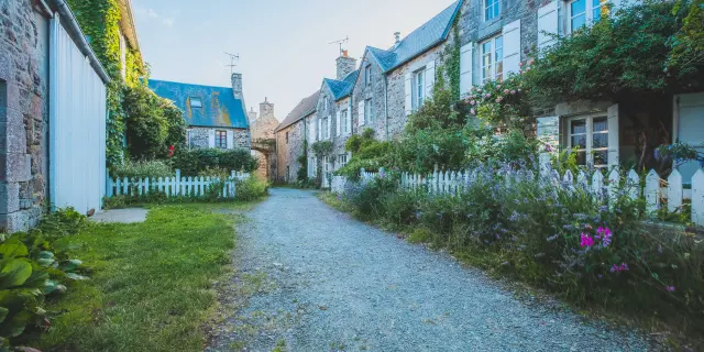 Rue pavée bordée de maisons en pierre avec des toits bleus et des jardins fleuris