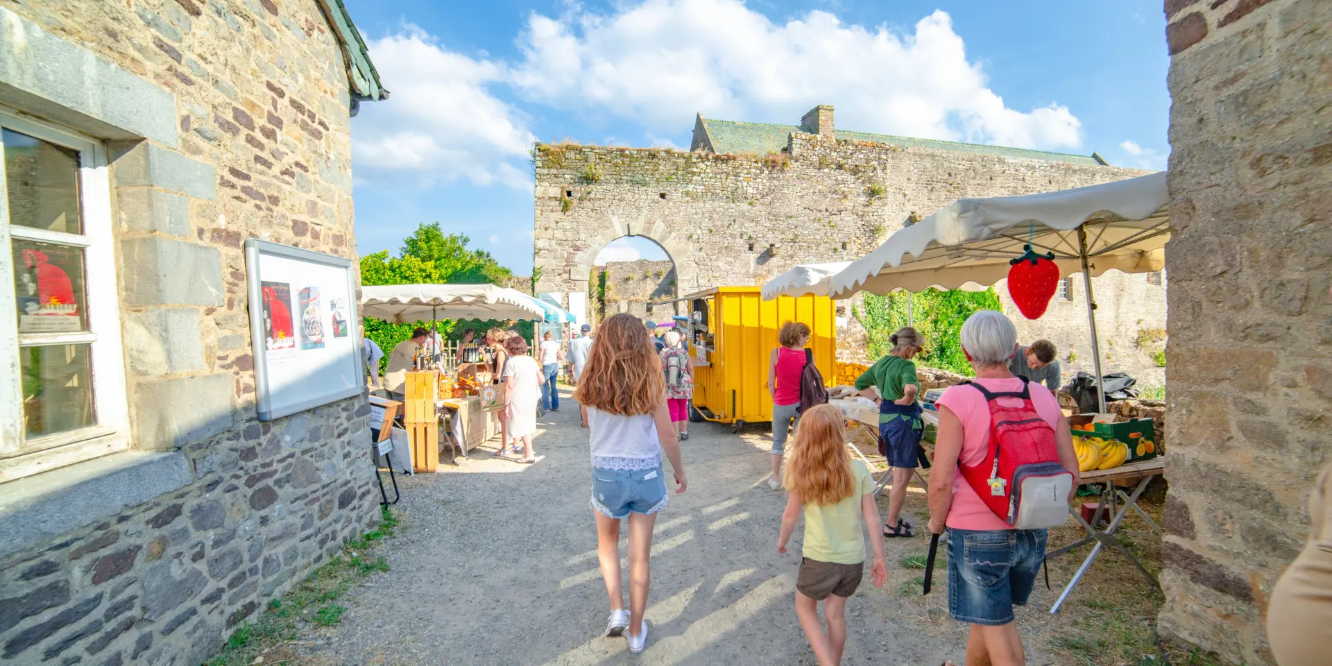 People walking in a historic market courtyard with stalls and stone buildings