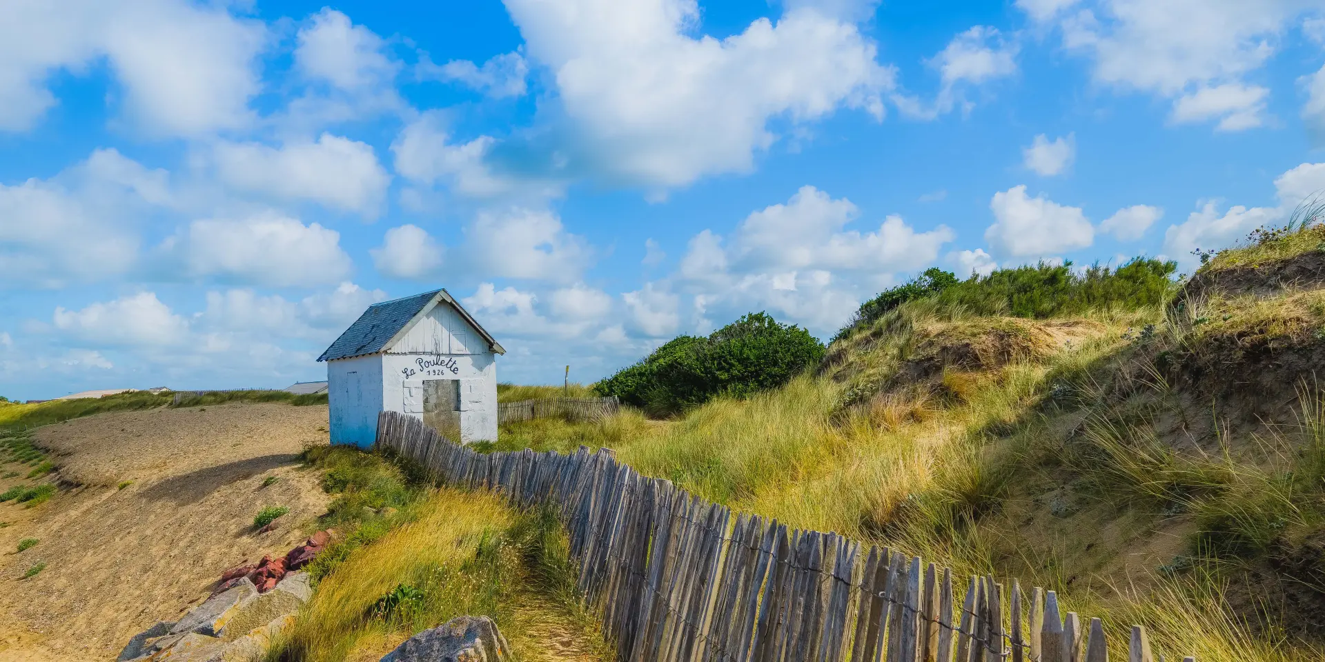 Kleine weiße Hütte am Strand mit einem Holzzaun