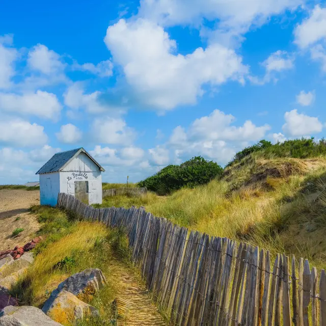 Kleine weiße Hütte am Strand mit einem Holzzaun