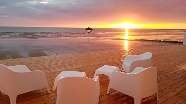 White chairs on a wooden terrace facing the sea at sunset