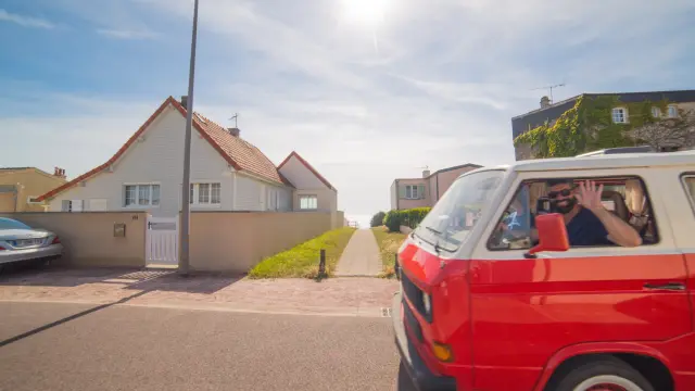 Un van rouge avec des personnes à l'intérieur, garé devant une maison blanche à Agon Coutainville