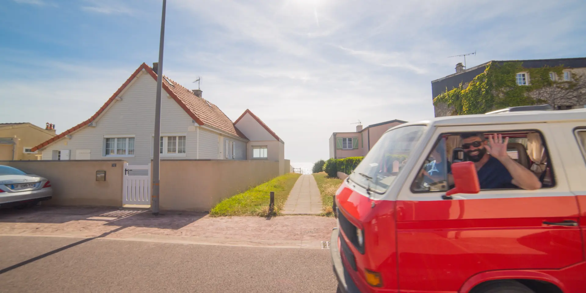 Un van rouge avec des personnes à l'intérieur, garé devant une maison blanche à Agon Coutainville