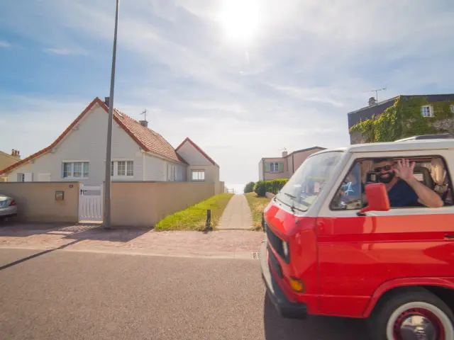 Un van rouge avec des personnes à l'intérieur, garé devant une maison blanche à Agon Coutainville