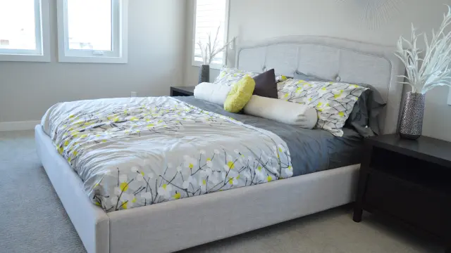 Chambre avec lit blanc, couvertures grises et jaunes, et deux tables de nuit