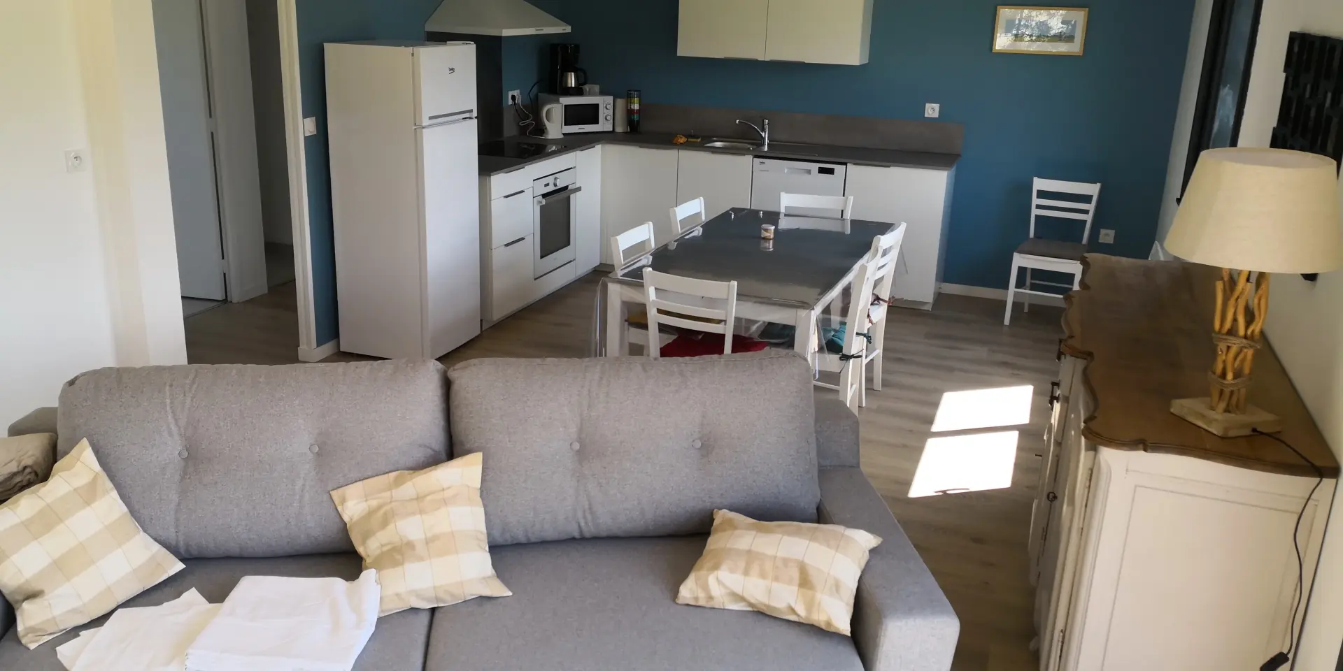 Moderner Innenraum mit Küche und Wohnzimmer, graues Sofa mit Kissen, Esstisch und Stühlen