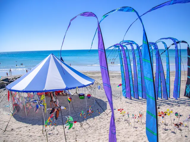 Drachenfest mit bunten Drachen und einem blauen Zelt am Strand