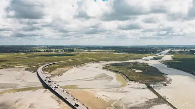 Holzbrücke über einen Sandstrand mit Menschen, die gehen