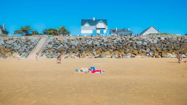 Kinder spielen an einem Strand mit einer Steinmauer und Häusern im Hintergrund