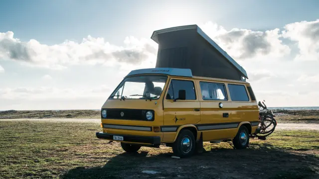 Ein gelber Wohnwagen mit aufgestellter Dachluke ist am Strand geparkt, daneben steht ein Fahrrad