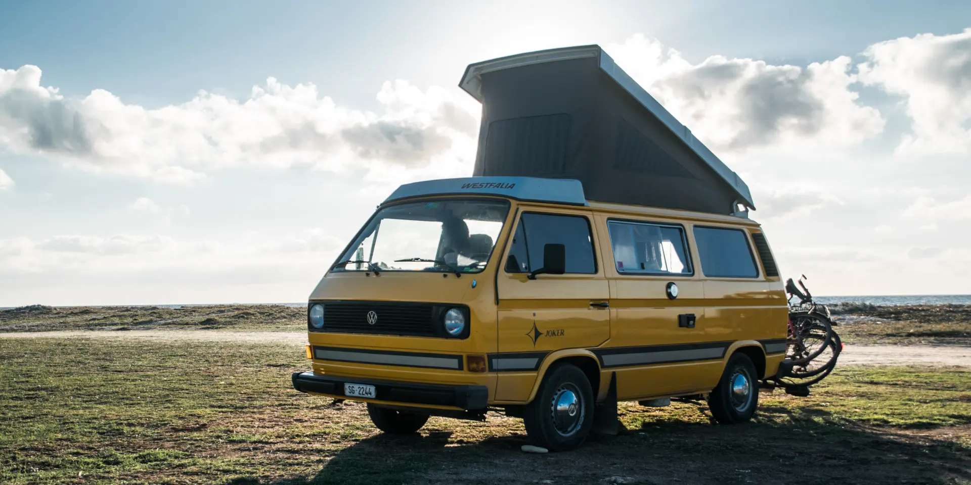 A yellow van with a raised roof is parked on a beach with a bicycle next to it
