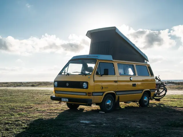 Un van jaune avec un toit relevé est garé sur une plage avec un vélo à côté