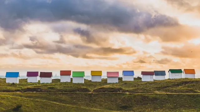 A row of colorful beach huts on a grassy hill at sunset