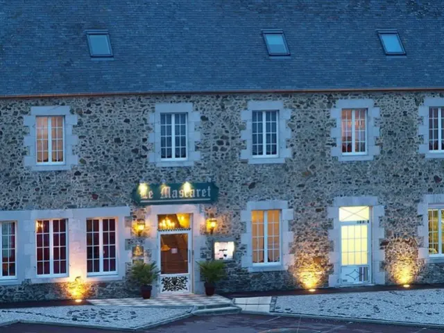 Facade of a stone hotel with lit windows and an entrance marked by a sign