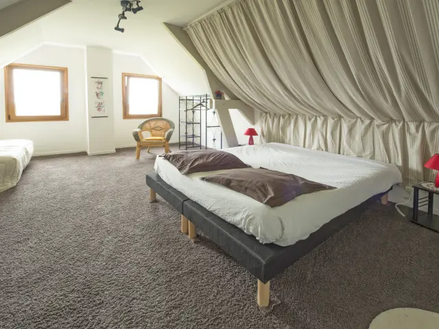 Dachkammer mit zwei Betten, weißen Vorhängen und minimalistischer Dekoration