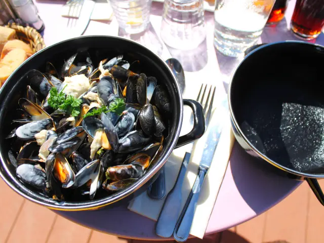 A pot of mussels marinières with open and closed shells, accompanied by parsley and bread