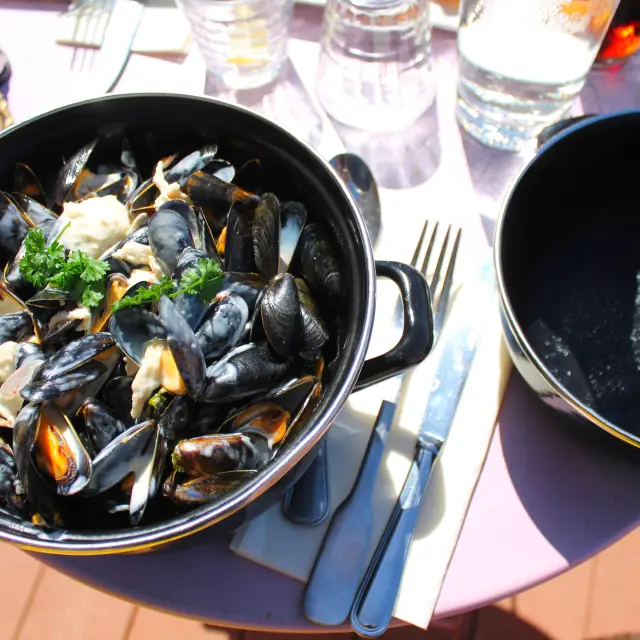 Un pot de moules marinières avec des coquillages ouverts et fermés, accompagné de persil et de pain