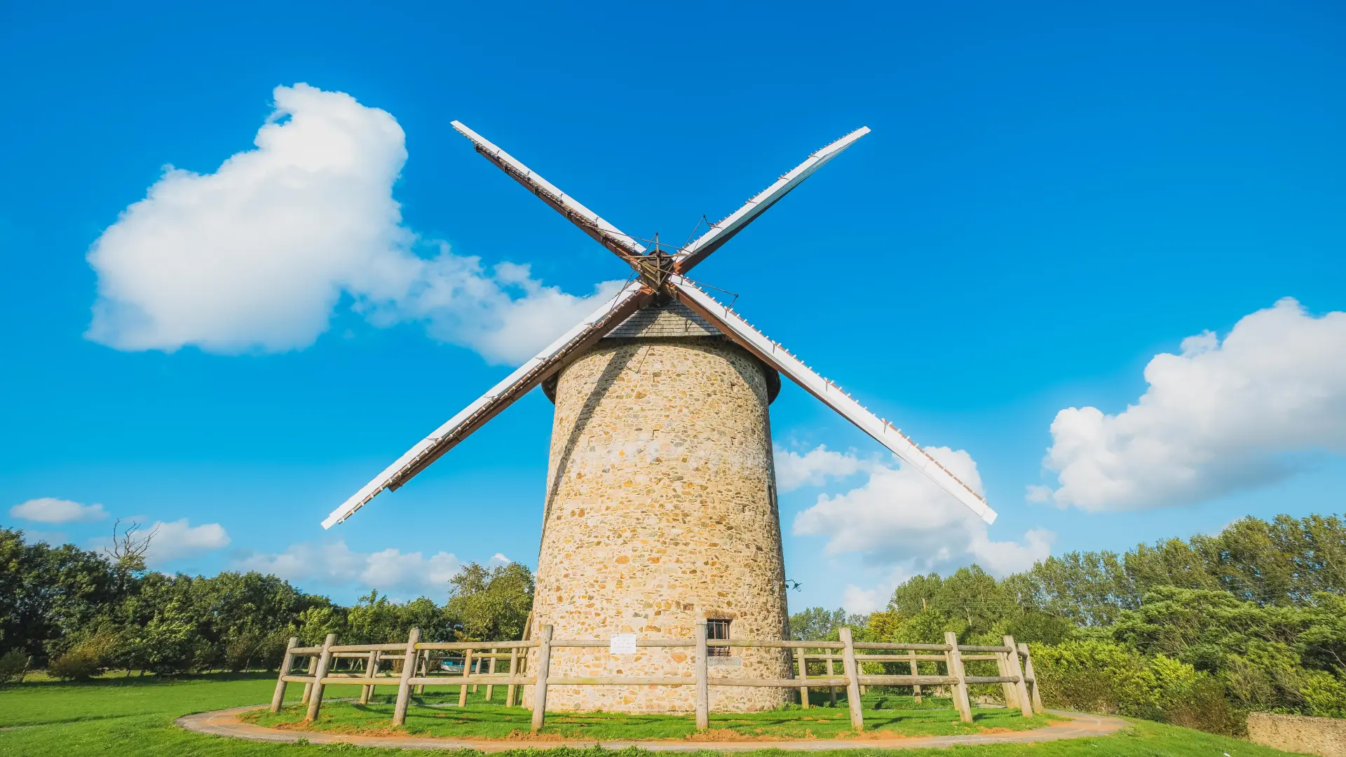 Un moulin à vent en pierre à Gouville sur Mer avec des ailes en bois sous un ciel bleu clair