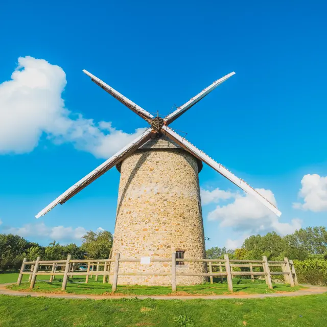 A stone windmill with wooden blades under a clear blue sky