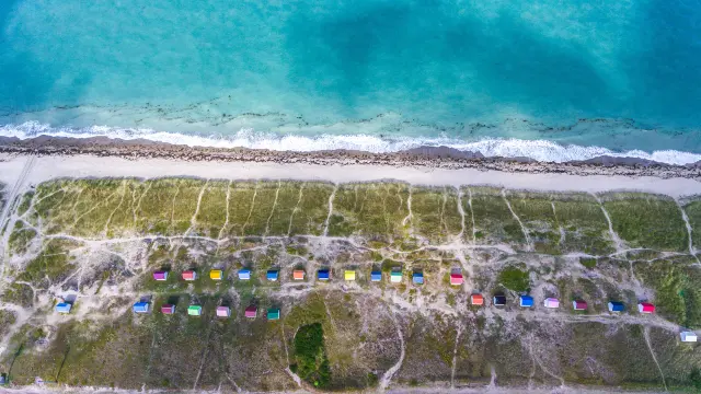 Weißer Sandstrand mit bunten Strandhütten und türkisfarbenem Meer