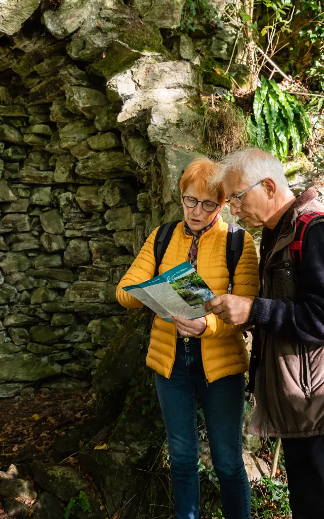 Deux randonneurs consultent une carte près d'un mur de pierre en pleine nature