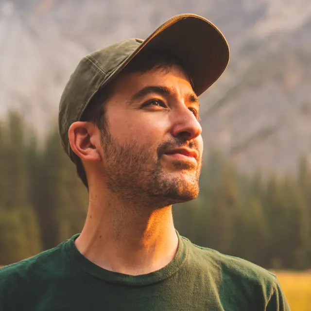 Un homme avec une casquette verte regarde au loin dans un paysage montagneux