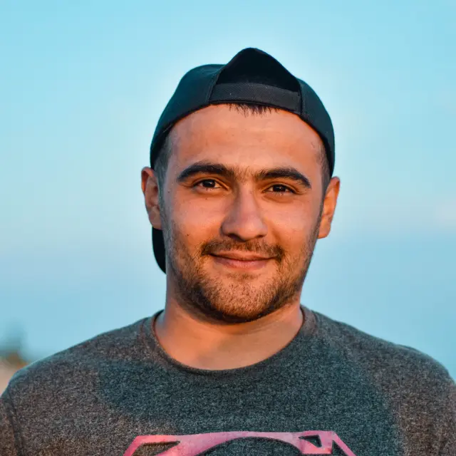Smiling man wearing a black cap and a gray t-shirt with a pink logo