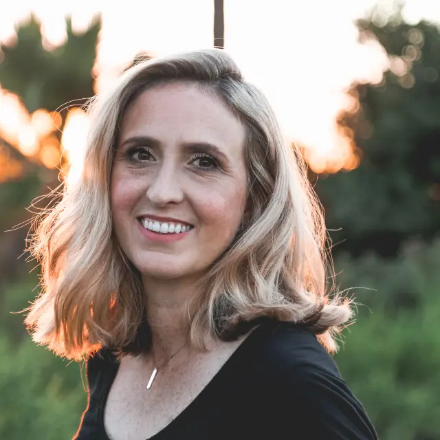 Smiling woman with blonde hair and a black t-shirt at sunset