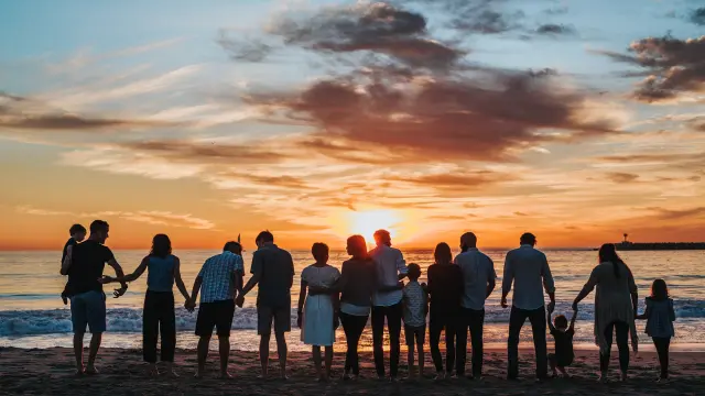 Une grande famille se tient sur une plage au coucher du soleil