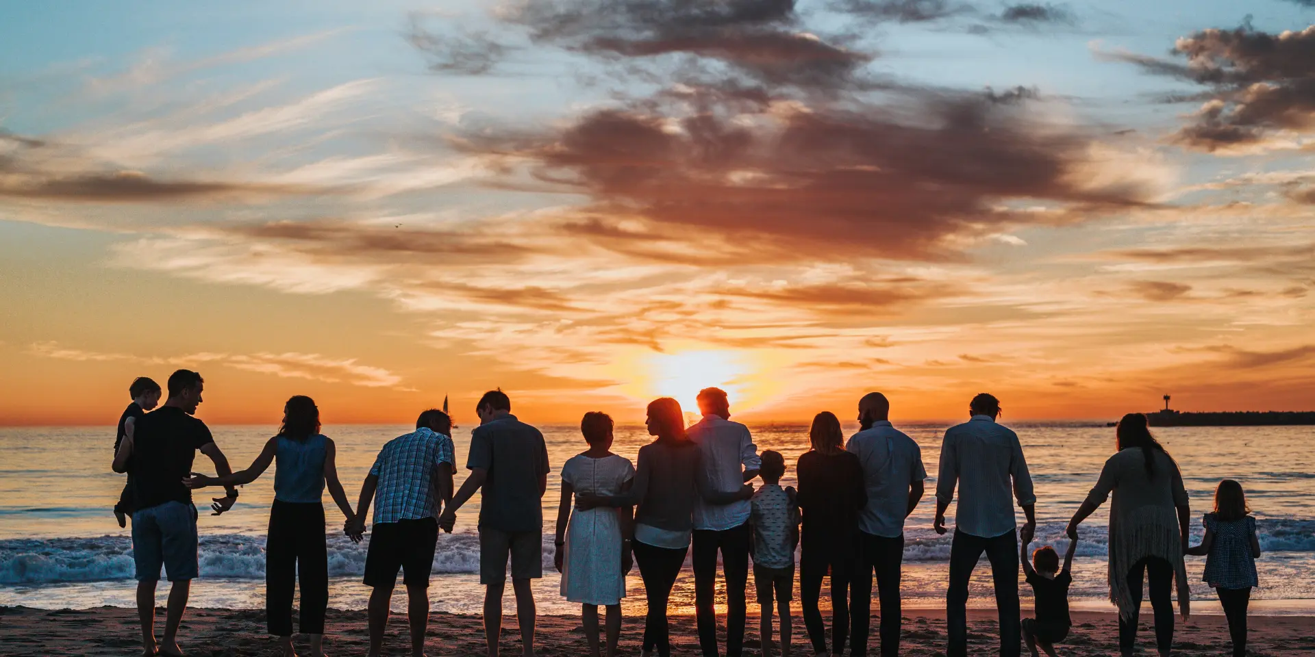 Une grande famille se tient sur une plage au coucher du soleil
