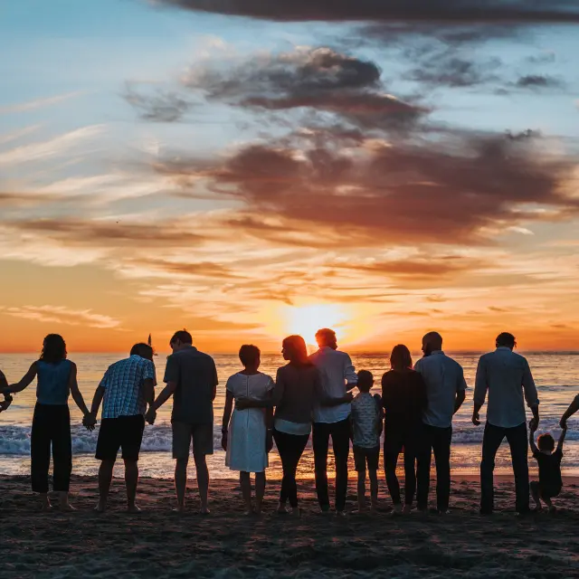 Une grande famille se tient sur une plage au coucher du soleil
