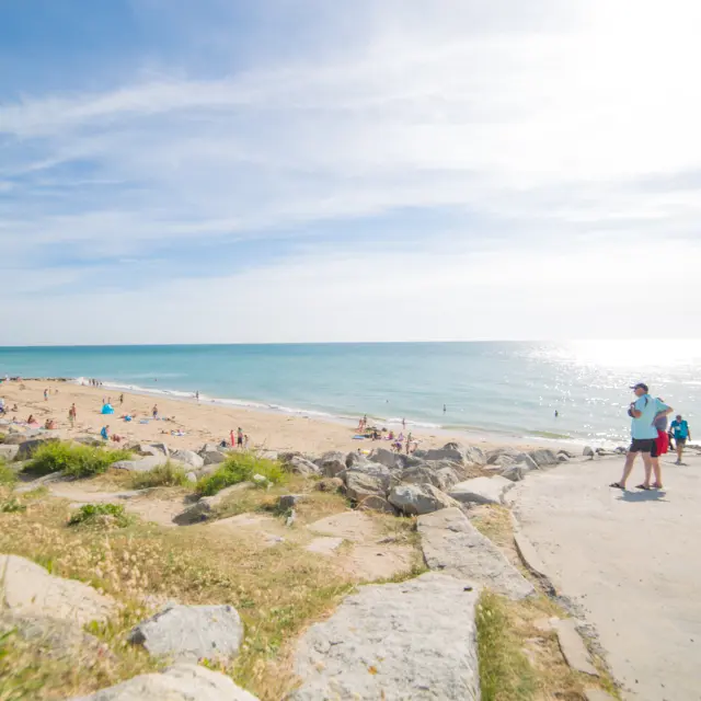 Gruppe von Menschen, die auf einem Küstenweg zu einem sonnigen Strand gehen