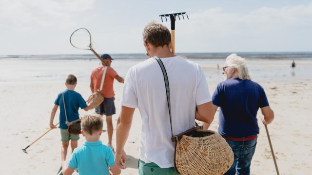 Une famille marchant sur la plage avec des outils pour chercher des coquillages