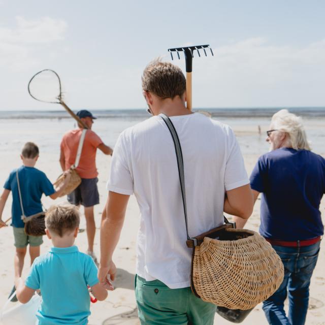 Une famille marchant sur la plage avec des outils pour chercher des coquillages