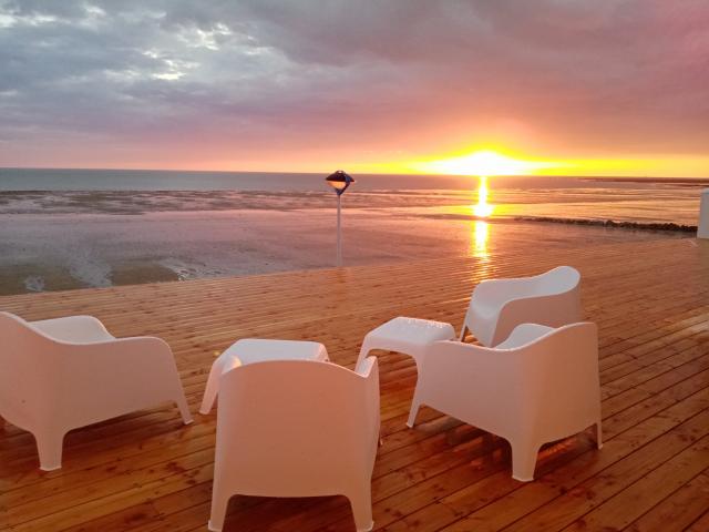 White chairs on a wooden terrace facing the sea at sunset