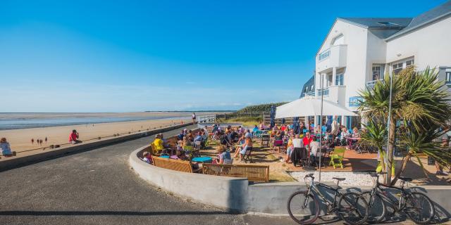 Crowded café terrace by the beach with people sitting and bicycles parked